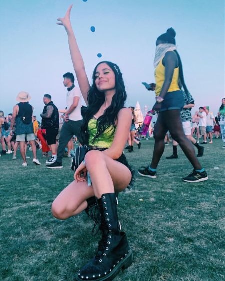 jenna in a green top black shorts and black boots holding up a peace sign 